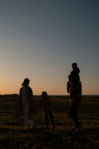 A family walking through a field at sunset, a child riding on a parent's shoulders