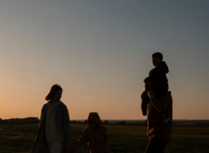 A family walking through a field at sunset, a child riding on a parent's shoulders