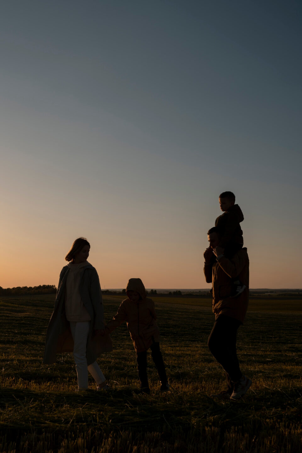 A family walking through a field at sunset, a child riding on a parent's shoulders