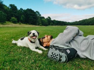 A person lying on the grass with a small dog beside them