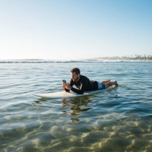 A surfer lying on his board on calm water, looking at his phone