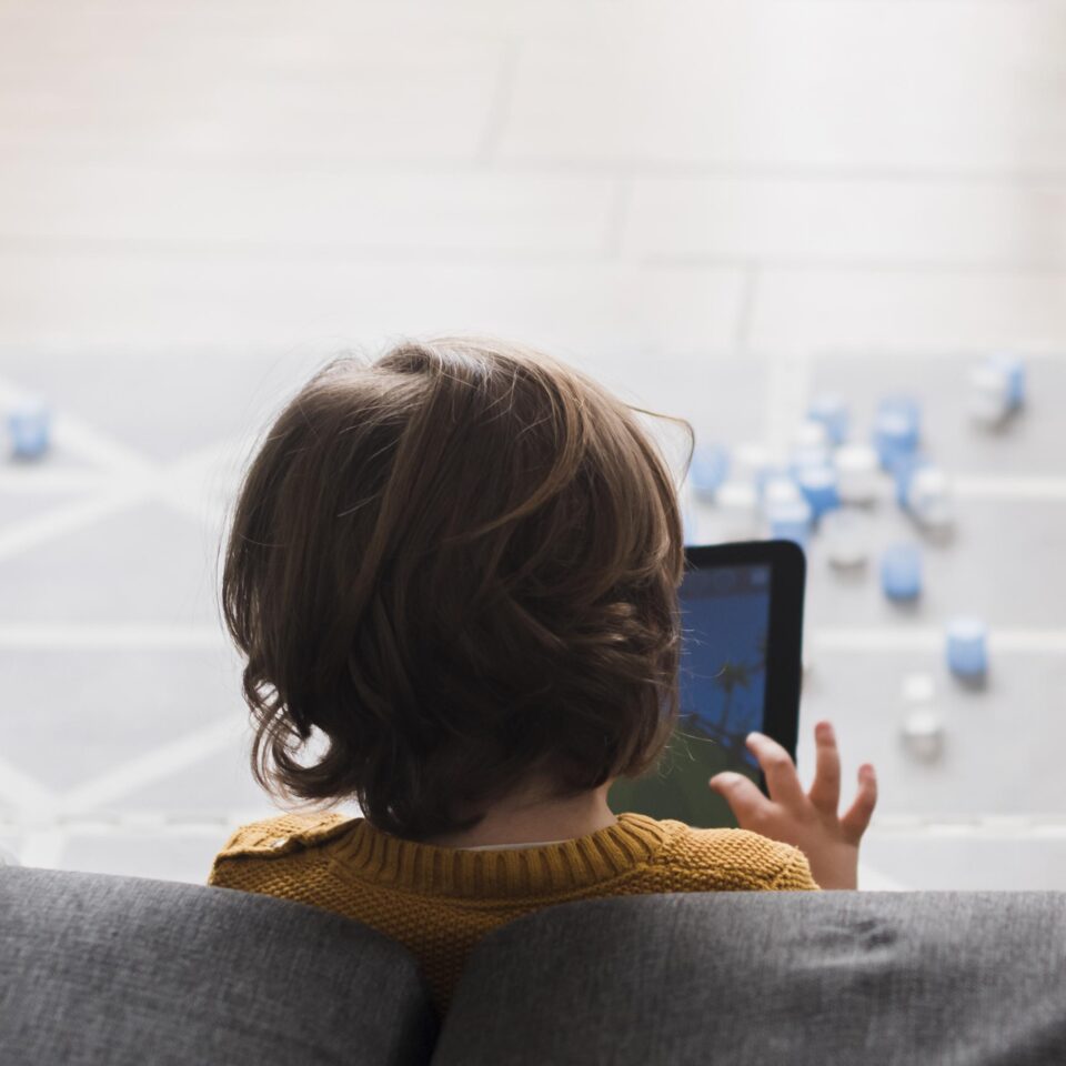 A child seen from behind, holding a tablet